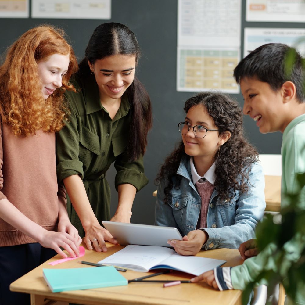 Zu sehen sind: eine Gruppe Kinder an einem Schreibtisch