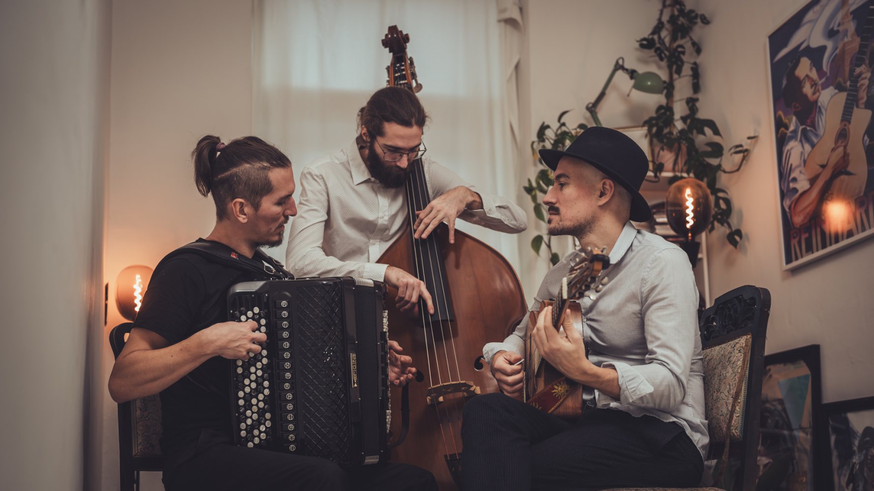 Auf dem Bild ist das Trio "Mosaic" aus der Steiermark zu sehen. Ein Mann spielt Gitarre, ein anderer Cello und der Dritte die Ziehharmonika. Die Farbharmonie des Bildes konzentriert sich auf die Farben Eierschale, Braun und Schwarz.